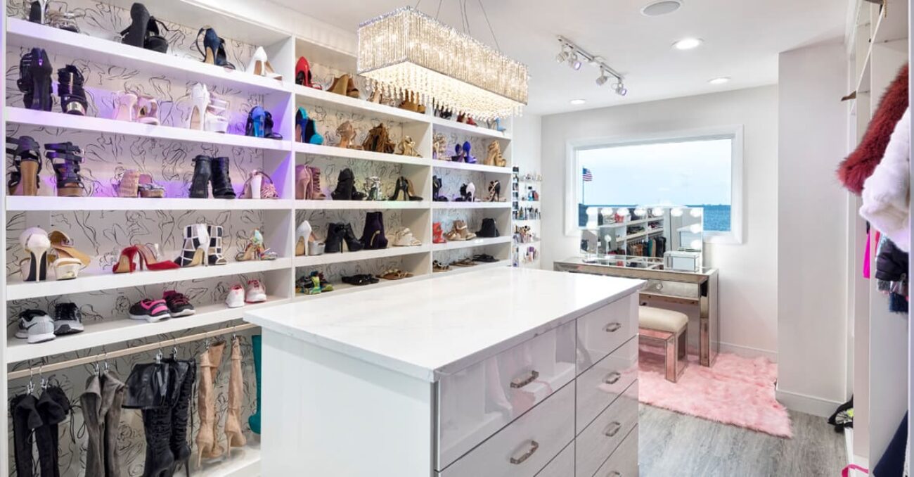 Closet featuring a large white island, wall of shelves for shoes and boots, and a sparkling chandelier.