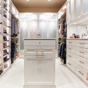 Custom walk-in closet with white built-in shelving, hanging rods, and LED rod lighting, featuring framed fronts and tray shelves for optimized clothing and shoe storage.