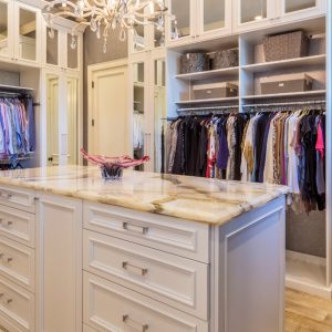 Mirror-front cabinets with integrated lighting, a center island with marble countertop, raised panel drawers, and fabric organizers for folded garments and accessories.