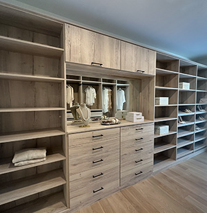 Modern walk-in closet featuring light wood cabinetry with open shelving