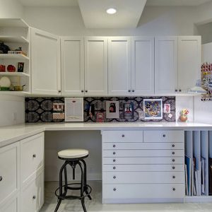 Craft White Chocolate Shaker cabinetry with flat file drawers, vertical paper slots, and a built-in pinboard backsplash. Includes overhead storage, open display shelves, and a dedicated sewing area.