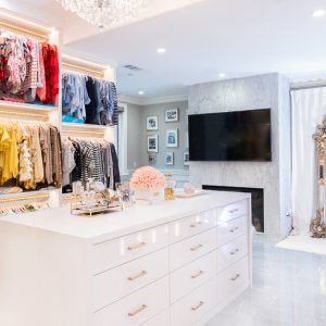 Boutique style dressing room with gold hanging rods, large center island with high gloss white drawer faces and fireplace