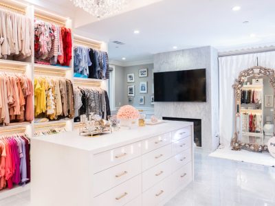 Boutique style dressing room with gold hanging rods, large center island with high gloss white drawer faces and fireplace