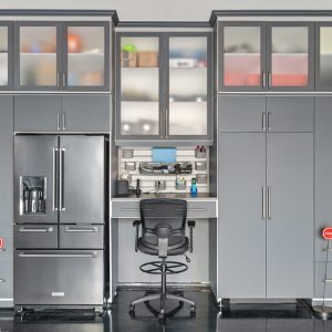 Sophisticated gray garage cabinetry system with a refrigerator, overhead frosted glass cabinets, and a central workstation