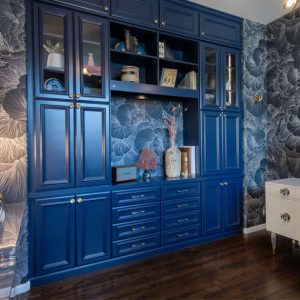 Bold home office built-in with deep blue shaker cabinetry, glass doors, crown molding, and display lighting
