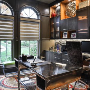 Sophisticated home office with dark wood cabinetry, metallic backsplash, under-cabinet lighting, and built-in cubbies for organized storage.