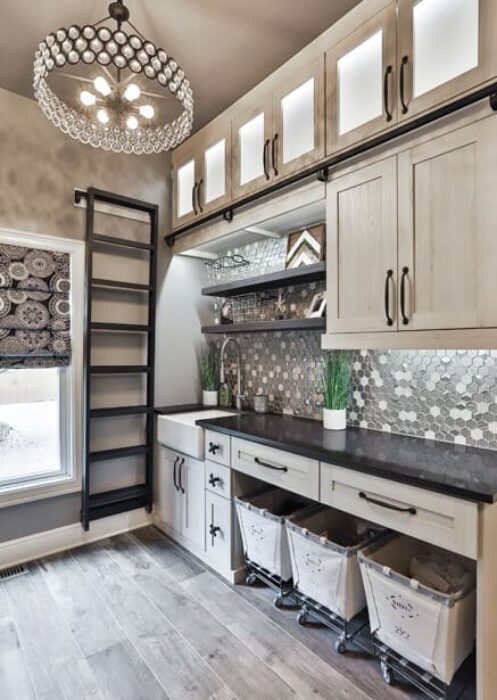 Elegant mudroom with upper glass-front cabinets, rolling ladder, mosaic tile backsplash, built-in laundry hampers, and shaker-style cabinetry.