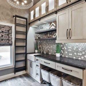 Elegant mudroom with upper glass-front cabinets, rolling ladder, mosaic tile backsplash, built-in laundry hampers, and shaker-style cabinetry.