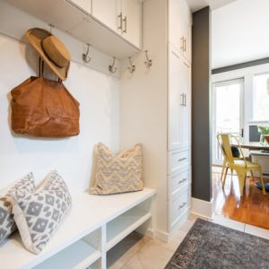 White mudroom built-in with hooks, a bench with pillows, upper cabinets, and a side drawer tower