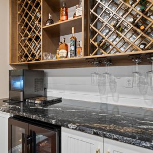 Wet bar with dark granite countertop, undercabinet wine fridge, stemware holders, and wooden lattice-style wine racks.