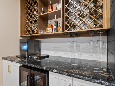 Wet bar with dark granite countertop, undercabinet wine fridge, stemware holders, and wooden lattice-style wine racks.