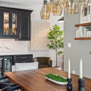 Sophisticated bar design in a dining space with glass-front black cabinets, white marble backsplash, dual beverage coolers, and decorative shelving.