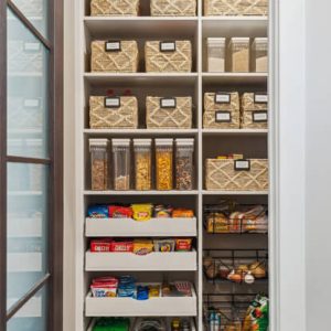 Narrow walk-in pantry optimized with labeled woven bins, cereal containers, snack drawers, and pull-out wire baskets for efficient small space storage.