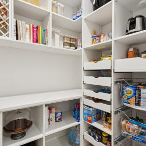 Organized white pantry with wine bottle storage, pull-out drawers, wire baskets, cookbooks, and countertop appliances.