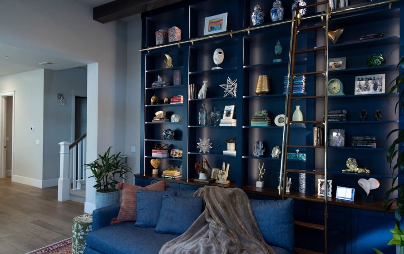 Floor-to-ceiling blue wall unit with brass rail ladder, open shelving
