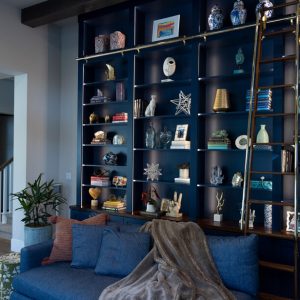 Floor-to-ceiling blue wall unit with brass rail ladder, open shelving