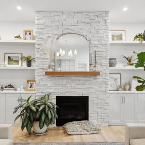 Symmetrical white wall unit with floating shelves and cabinetry flanking a stacked stone fireplace