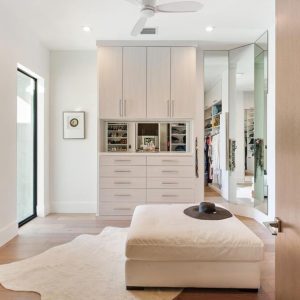 Contemporary wardrobe closet with slab front cabinet doors and drawers. The central built-in unit features mirrored cubbies with velvet-lined necklace organizers.