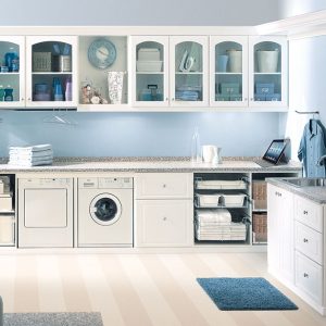 Custom laundry room cabinetry with glass door fronts, pull-out wire baskets, hanging rods, integrated laundry sink, and folding station.