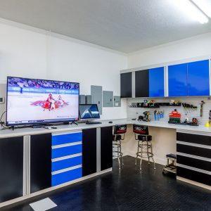 Man cave & garage combination with open shelving unit, slatwall tool storage, high gloss dual-tone cabinetry and drawers with sleek metallic pulls.