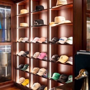 Sophisticated wardrobe suite with floor-to-ceiling fluted glass doors, wraparound cabinetry, and built-in hat display shelving with integrated lighting.