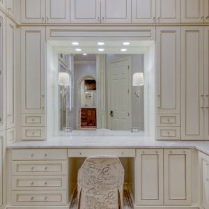 Full vanity suite built into a dressing room with glass insert cabinet doors and integrated lighting surrounding mirror.
