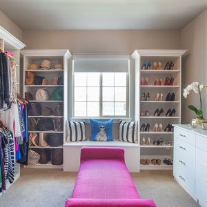Walk-in closet with dual hanging rods, crown molding, built-in drawers and window seat bench.